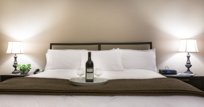 Two wine glasses and a bottle in the tray placed on the bed